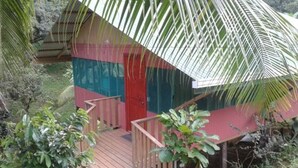 A small, single-story structure with a red door and a green and blue exterior. - Drake Lapas (Drake Bay)