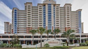 A multi-story hotel with a central atrium, balconies, and a sign indicating it is a condominium. - Lighthouse 801 Corner Unit Beachfront w HUGE wrap balcony! Book for Aug., Fall! (Gulf Shores)