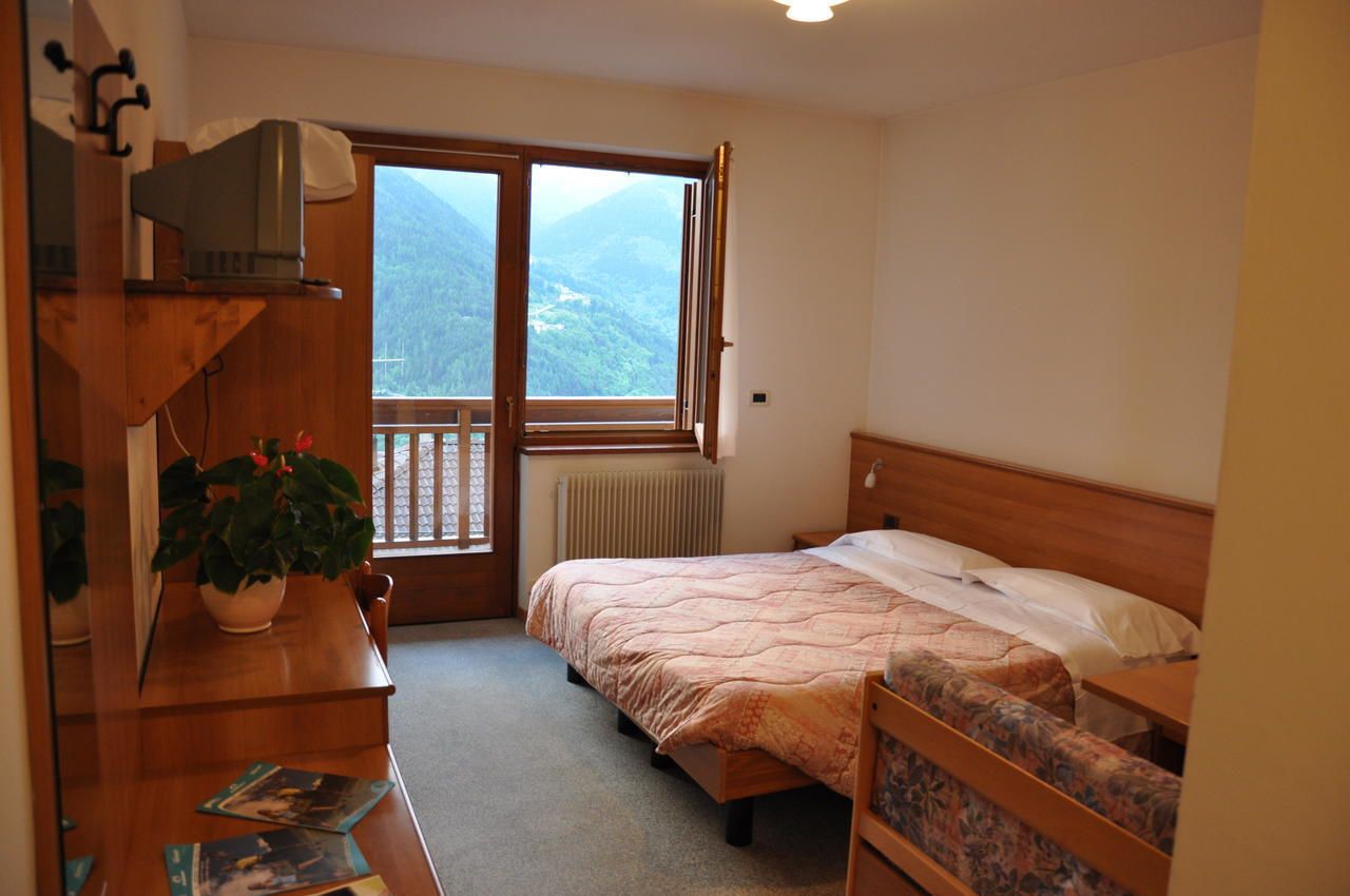 A bedroom with a bed, a wooden desk, a potted plant, and a window with a view of mountains.