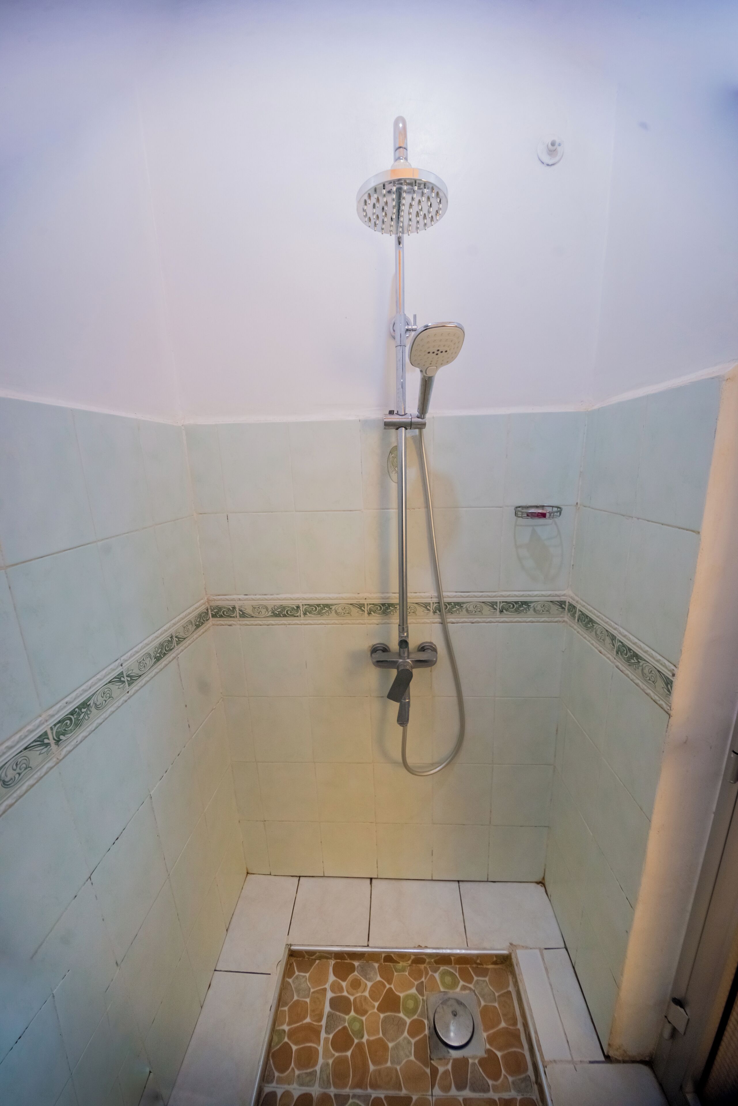 Ducha con cabezal de ducha de mano y grifo empotrado en un baño con azulejos.