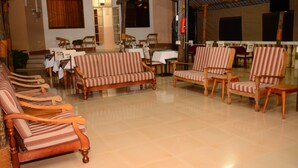 A spacious lobby with striped sofas, wooden chairs, and tables set up for dining. - Mama Thea Homes - Hostel (Moshi)