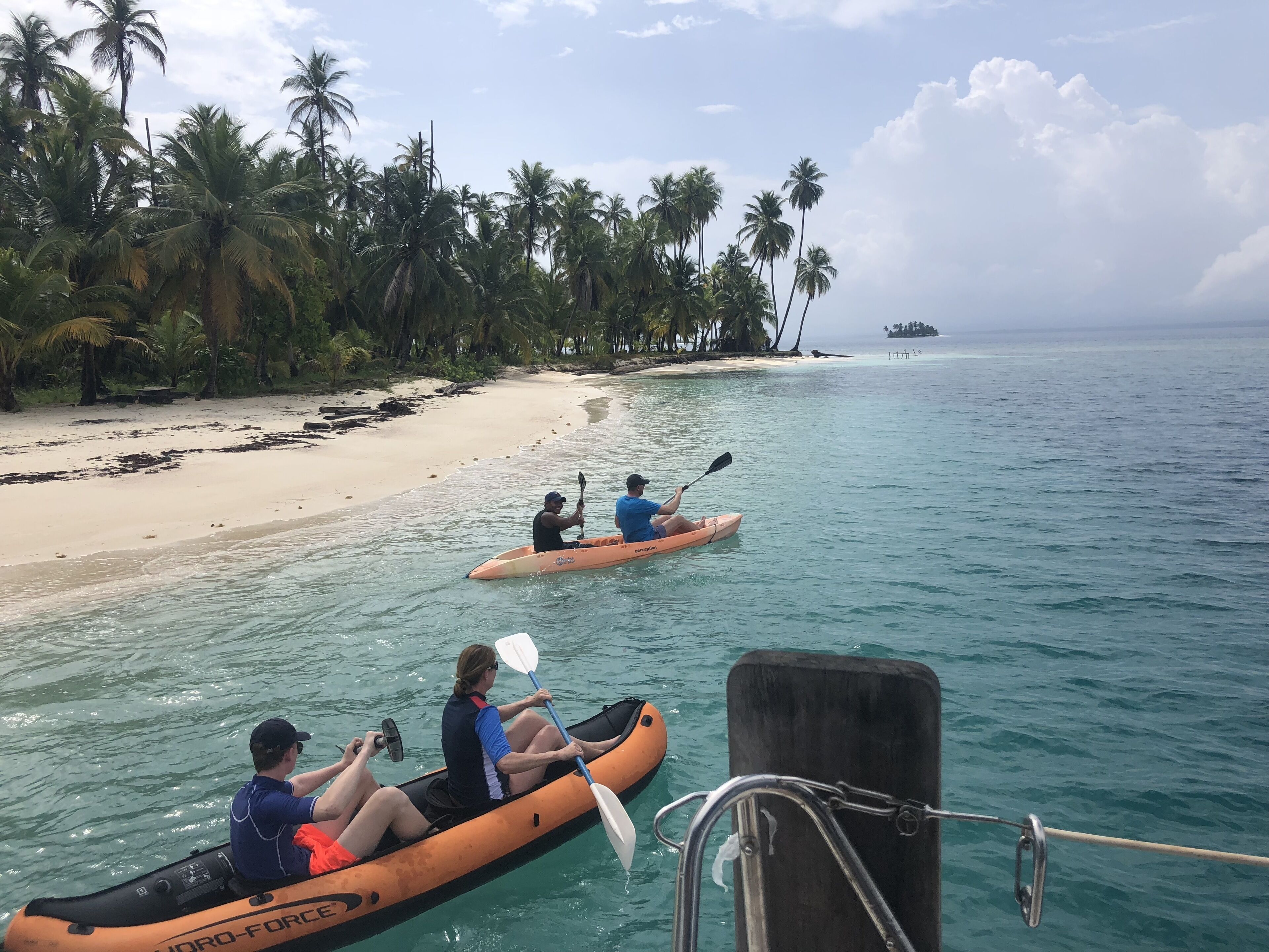 A beach with clear turquoise waters, a sandy shore lined with palm trees, and kayaks in the water.
