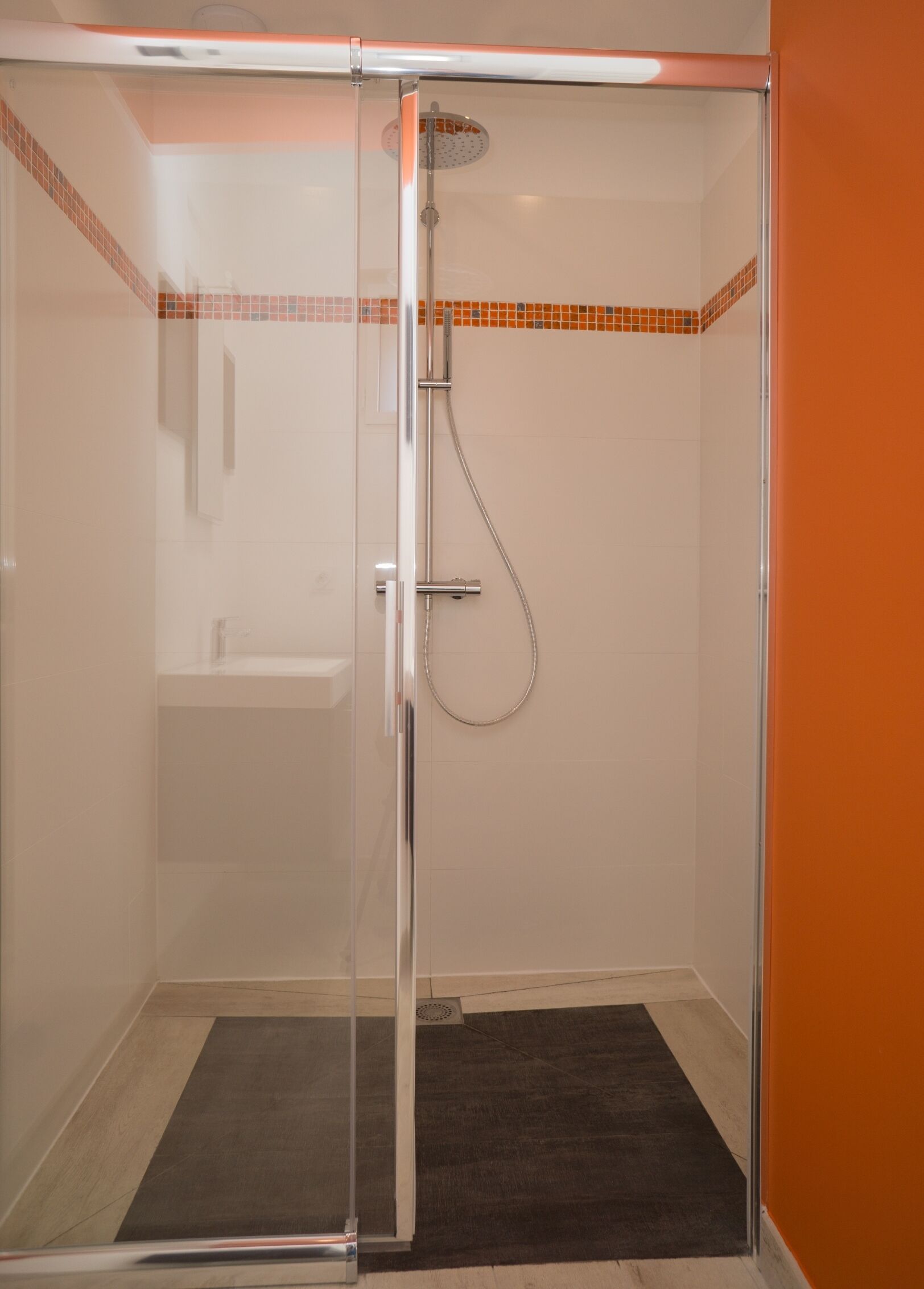 A glass-enclosed shower with a handheld showerhead and a wall-mounted faucet.