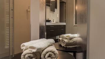 A modern bathroom with a glass shower enclosure, a dark vanity with a mirror, and neatly folded towels on a round table.