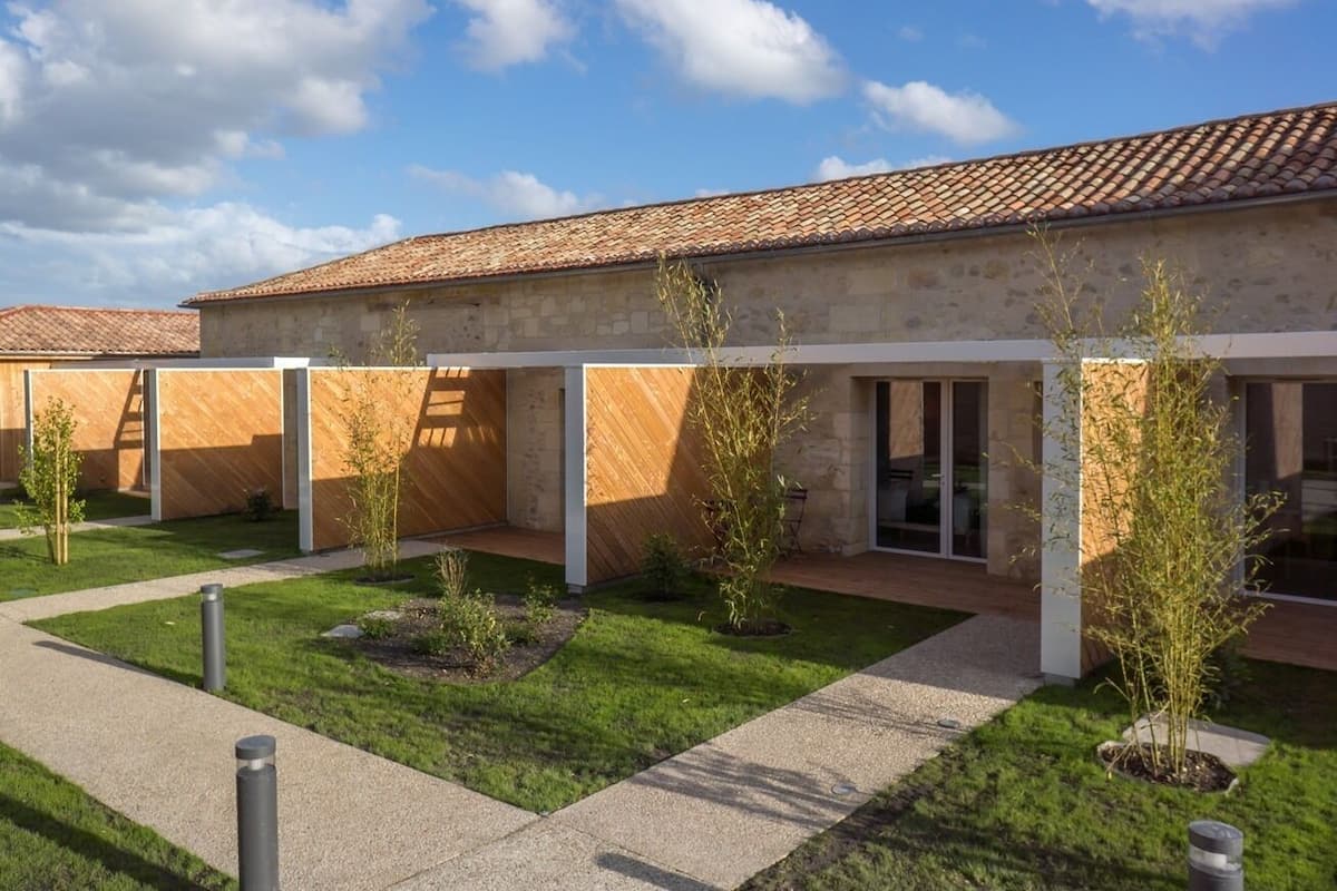 A modern building with a tiled roof, covered outdoor seating area, and a well-maintained garden with small trees and shrubs.