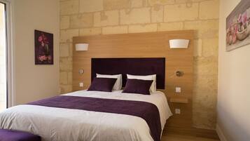 A bedroom with a wooden headboard, two bedside tables, a bed with white and purple bedding, and a brick wall.