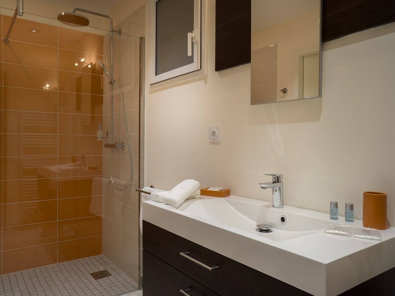 A modern bathroom with a glass shower enclosure, a white sink, and a dark vanity.