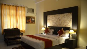 A hotel room with a large bed, two bedside tables with lamps, a sofa, a patterned rug, and a painting on the wall. - Ranthambore City Heart (Sawai Madhopur)