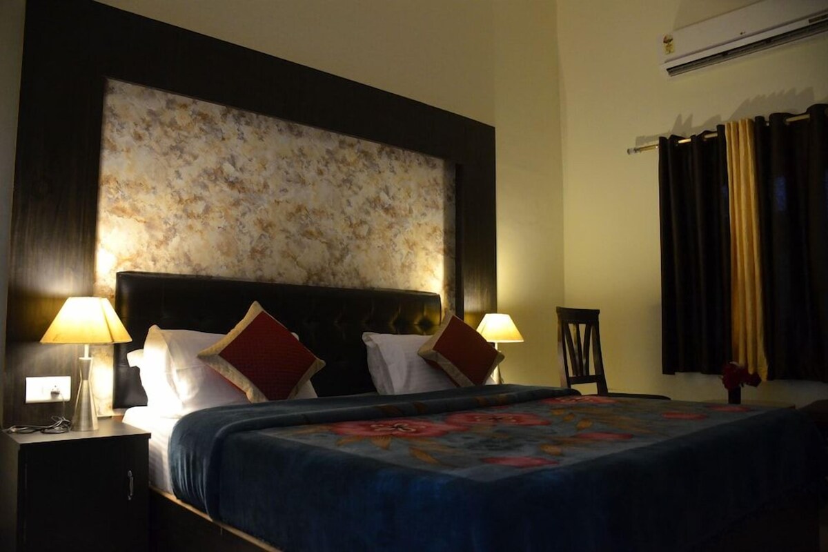Ein Hotelzimmer mit einem großen Bett, zwei Nachttischlampen, einem Kopfteil und einer Wand mit Struktur darüber sowie einem Fenster mit Vorhängen.