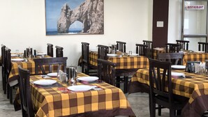 A restaurant with checkered tablecloths, wooden chairs, and a painting of a rock formation on the wall. - Ranthambore City Heart (Sawai Madhopur)