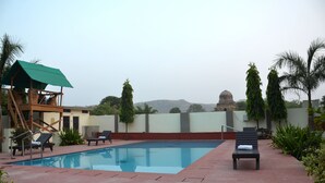 A swimming pool with lounge chairs and a covered seating area. - Ranthambore City Heart (Sawai Madhopur)