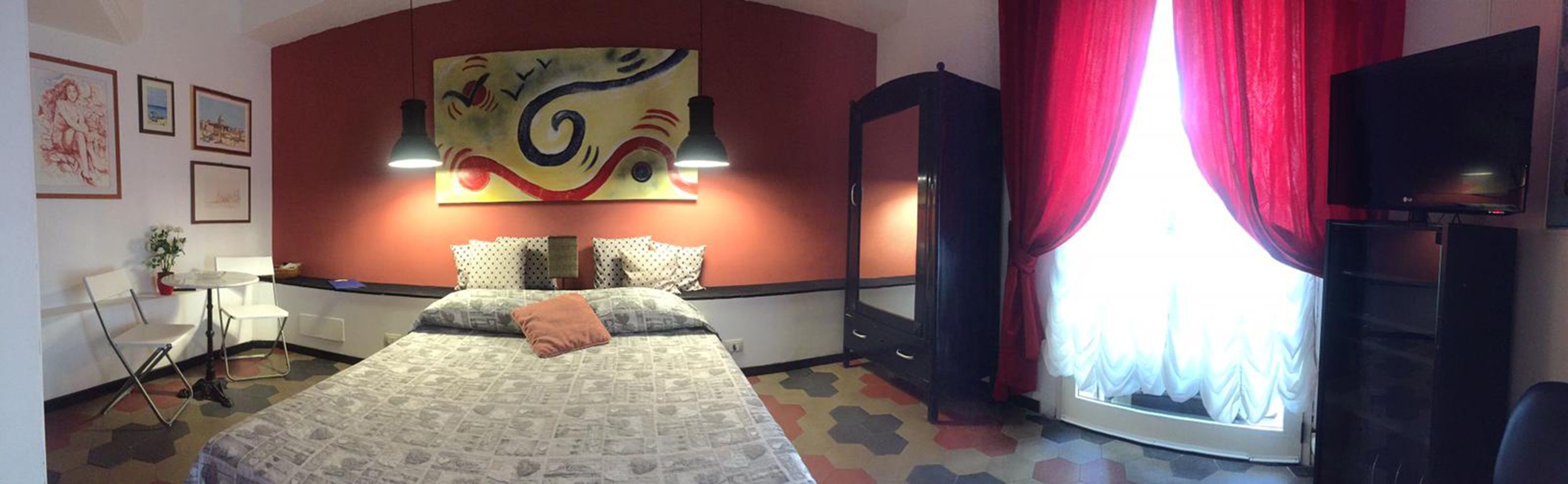 Habitación de hotel con cama, escritorio, silla, televisor y un ventanal con cortinas.