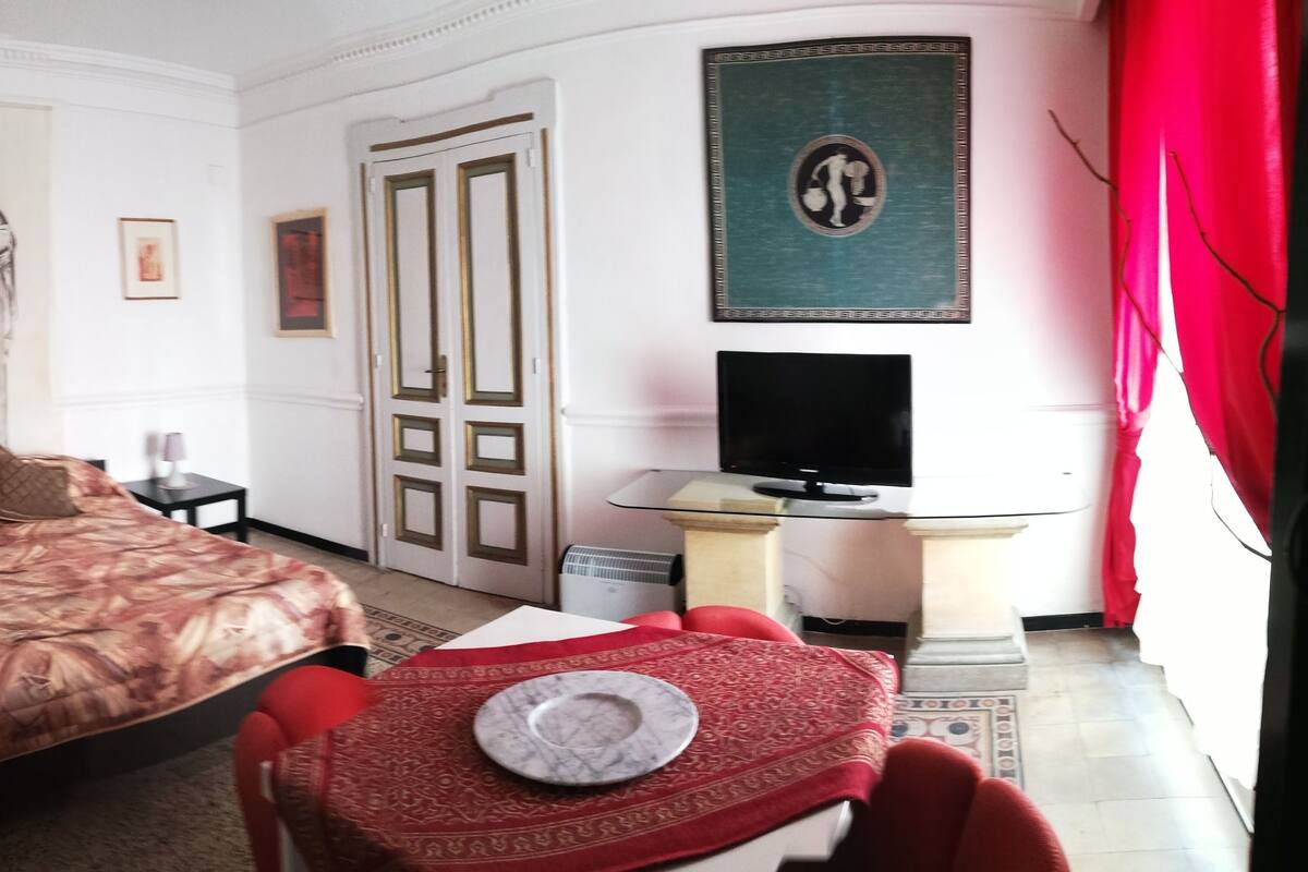 Una habitación de hotel con una cama, un televisor, una silla roja y un cuadro grande en la pared.