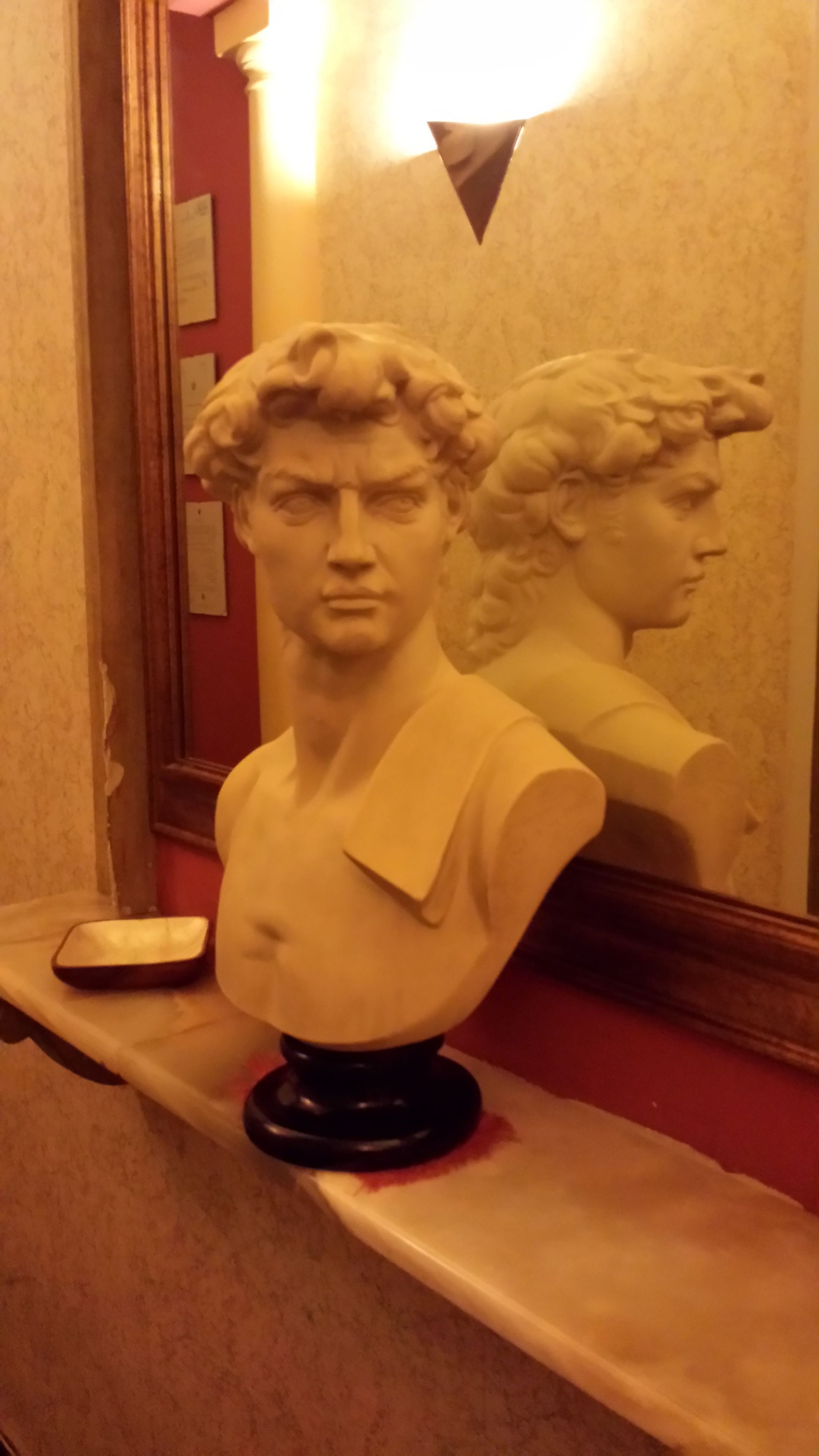 A bust sculpture on a shelf with a mirror reflecting it.