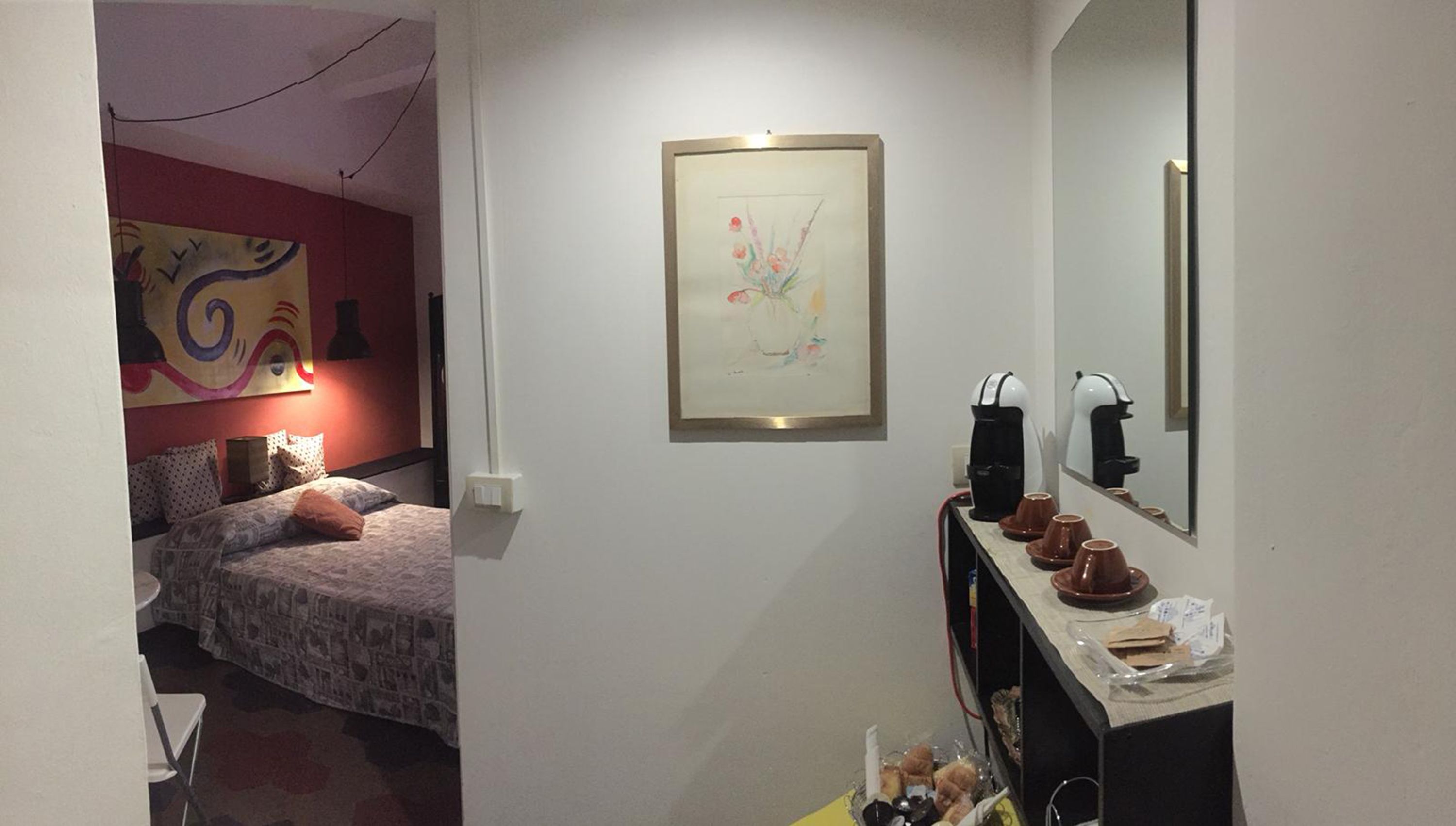 Une petite chambre à coucher accueillante, avec un lit, une table de chevet dotée d’un miroir et un tableau accroché au mur.