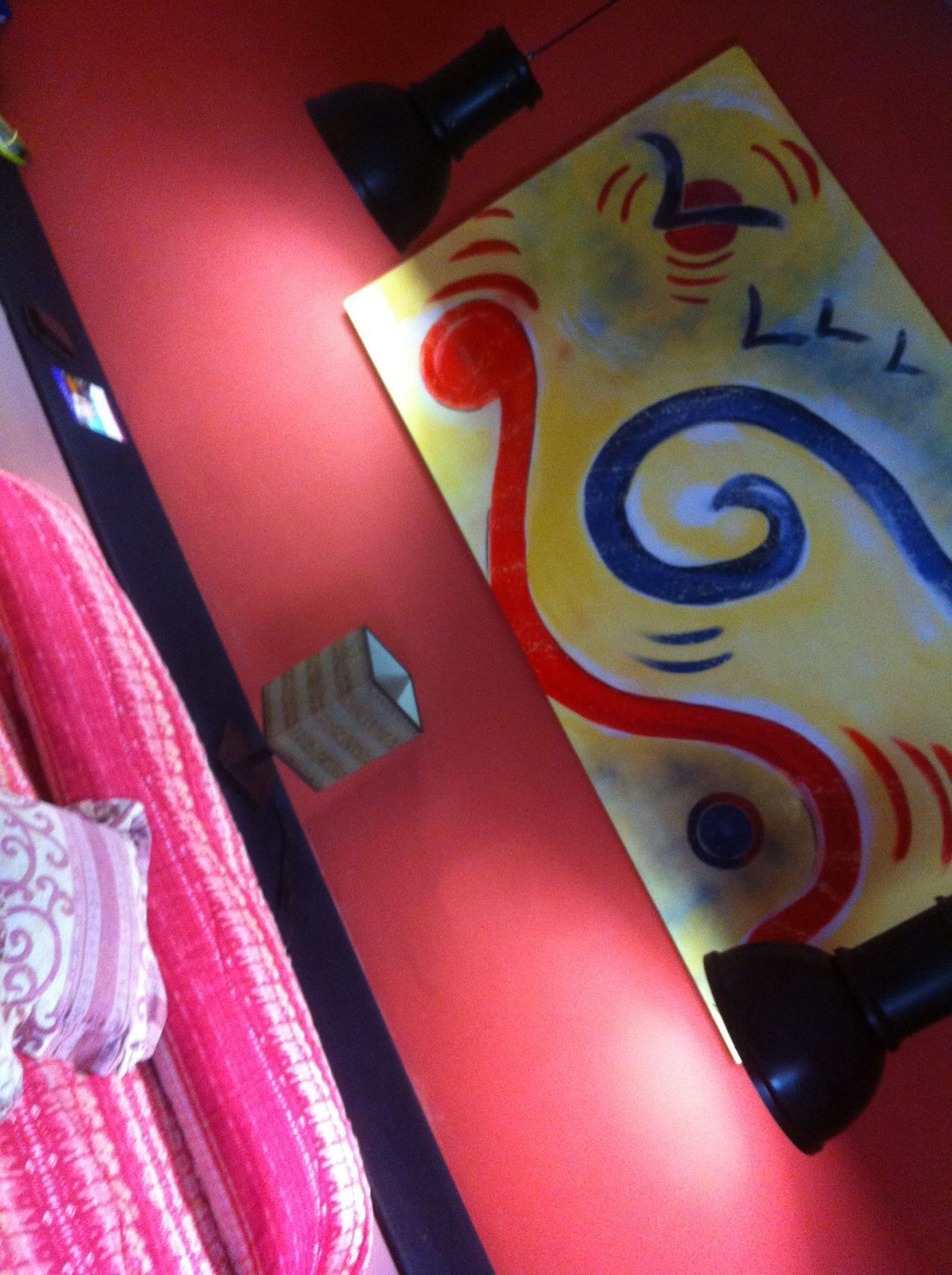 Un mur rouge orné d’un tableau abstrait aux couleurs vives et d’une lampe noire.