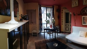 A living room with a white sofa, a dining table with chairs, a kitchen area with a white cabinet, and a window with curtains.