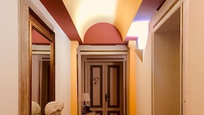 A hallway with a marble bust, a door with a mirror, and a red carpet.