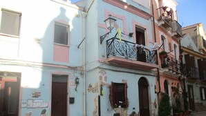 A multi-story building with a pink and blue facade, balconies with wrought iron railings, and potted plants. - L'Antica Locanda (Iglesias)