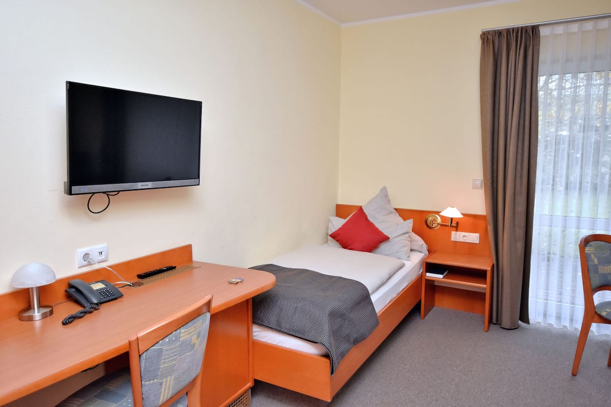 A hotel room with a bed, a desk with a telephone, a television mounted on the wall, and a window with curtains.
