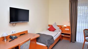 Habitación de hotel con una cama, un escritorio con teléfono, un televisor en la pared y una ventana con cortinas.