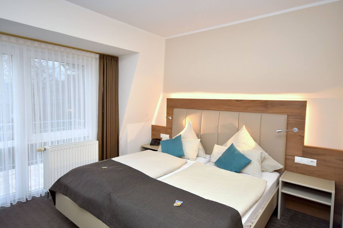 A hotel room with a large bed, a wooden headboard, and a bedside table with a lamp.