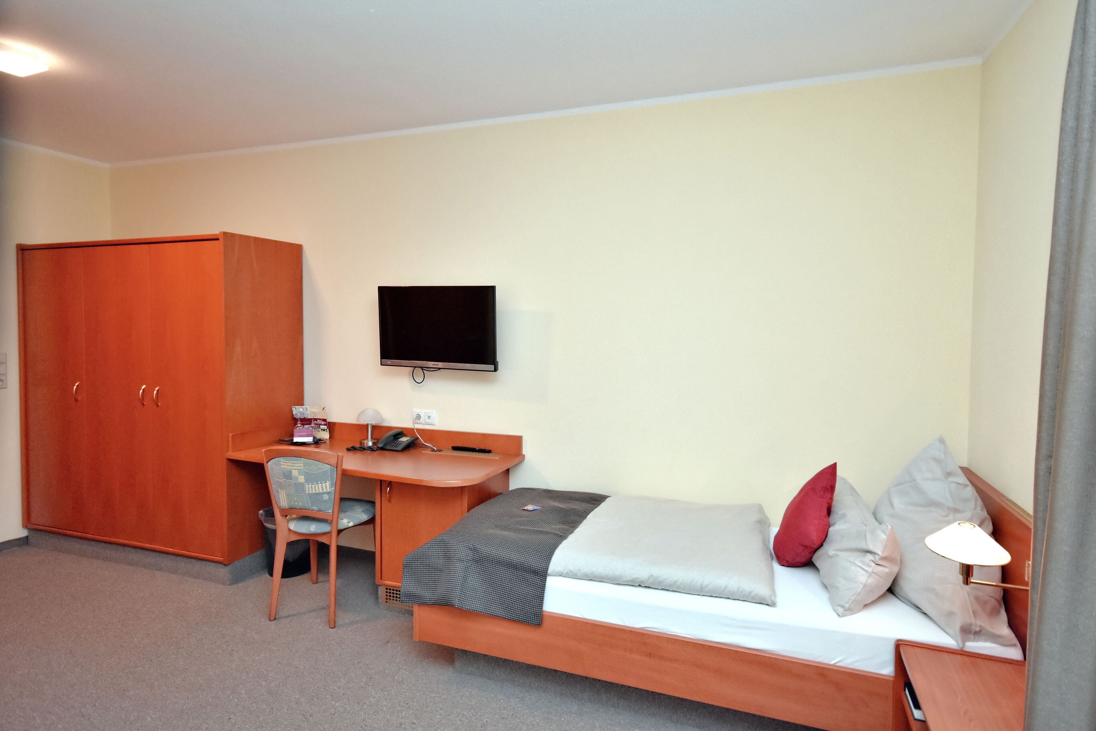 A compact hotel room with a single bed, a desk with a chair, a television, and a wardrobe.