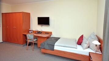 A compact hotel room with a single bed, a desk with a chair, a television, and a wardrobe.