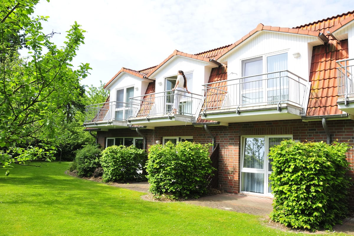 A two-story house with a brick facade, a balcony on the second floor, and a well-maintained lawn.