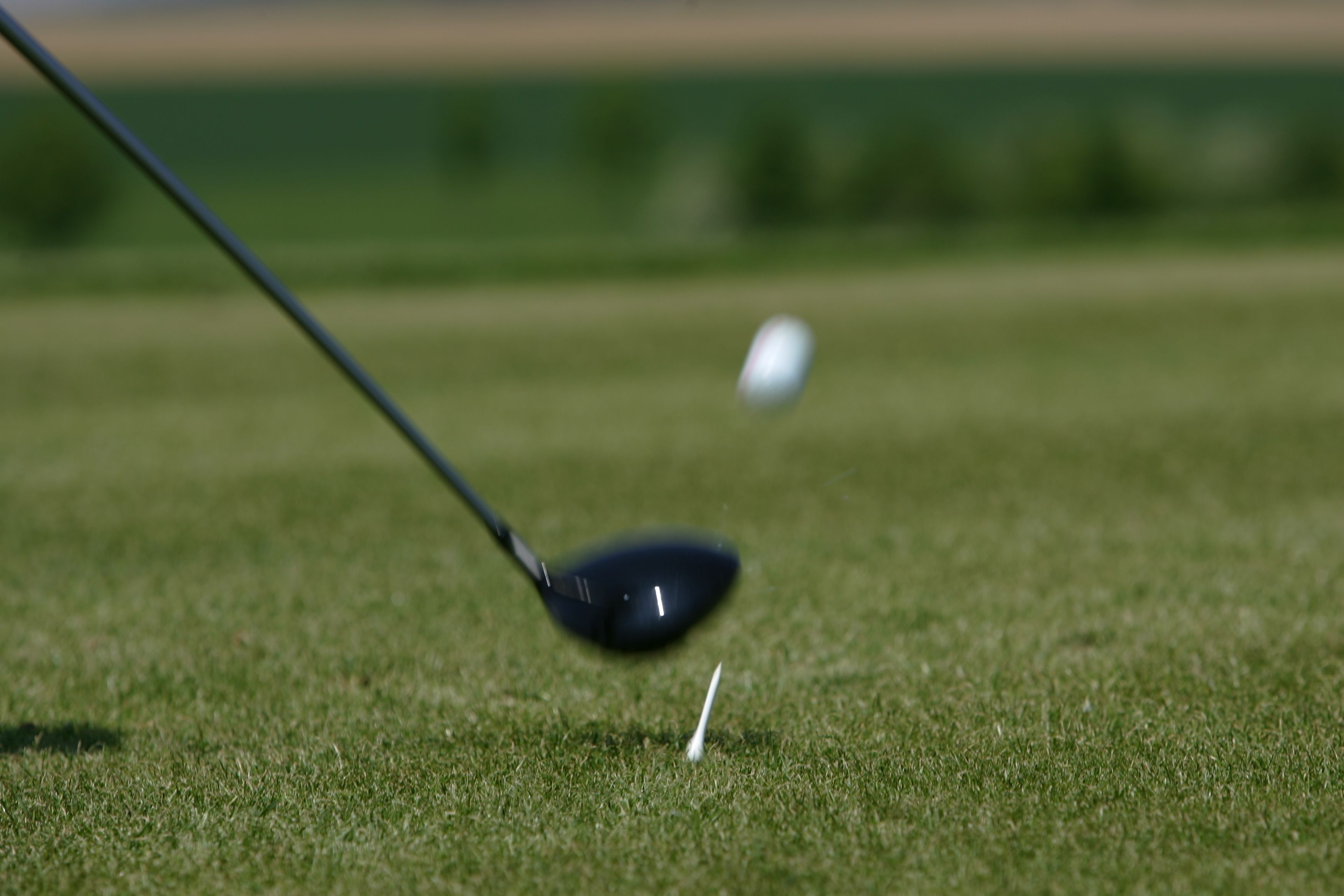 A golf club in motion on a green, with a golf ball in the background.