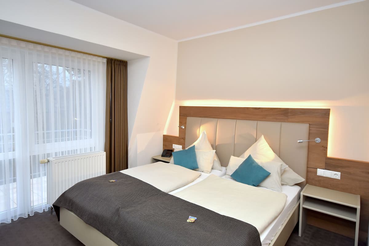 A double bed with a wooden headboard, bedside tables, and a window with sheer curtains.