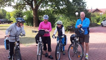 Four people on bicycles on a paved path with trees and a building in the background.
