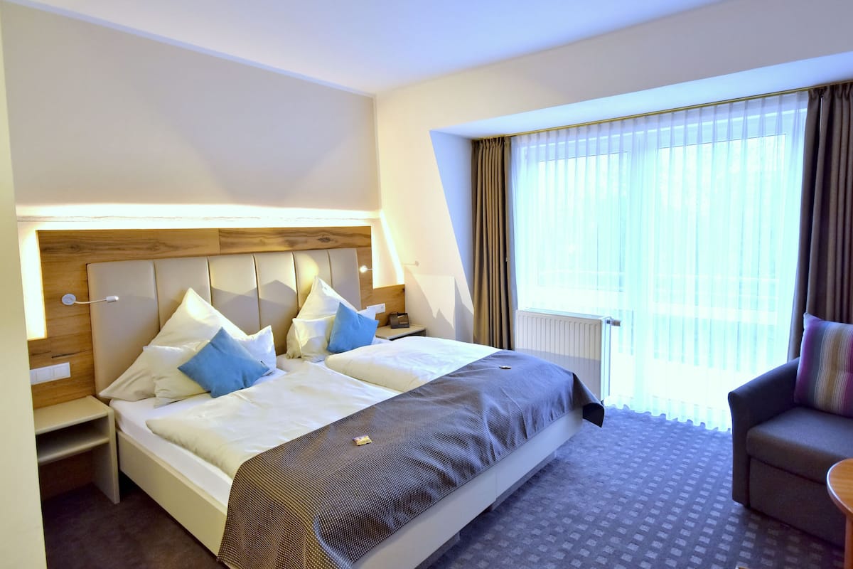 A hotel room with a large bed, a sofa, a nightstand, and a window with curtains.