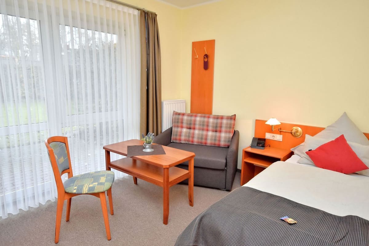 A hotel room with a bed, a sofa, a chair, a small table, and a nightstand.