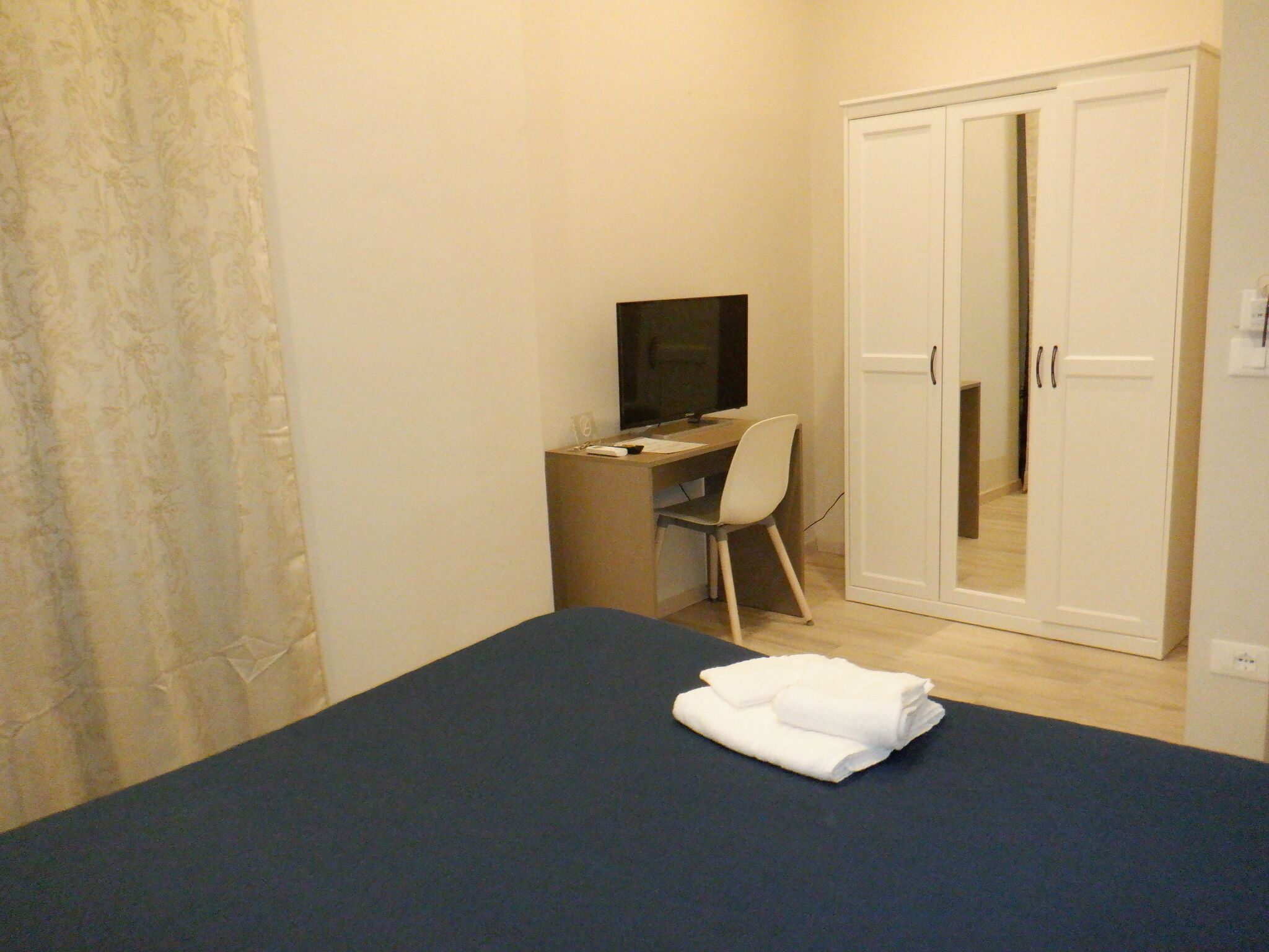 A bedroom with a bed, a desk with a chair, a TV, and a wardrobe.