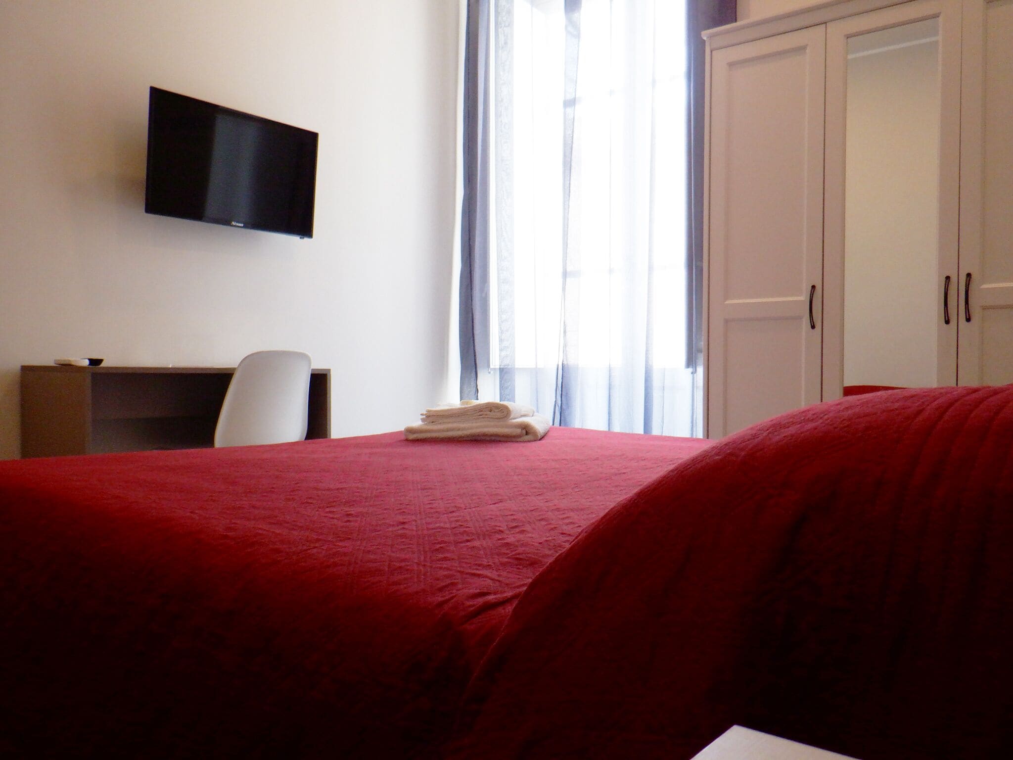 Une chambre d’hôtel équipée d’un lit, d’un bureau, d’une chaise, d’un téléviseur fixé au mur et d’une armoire.
