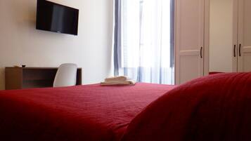 Une chambre d’hôtel équipée d’un lit, d’un bureau, d’une chaise, d’un téléviseur fixé au mur et d’une armoire.