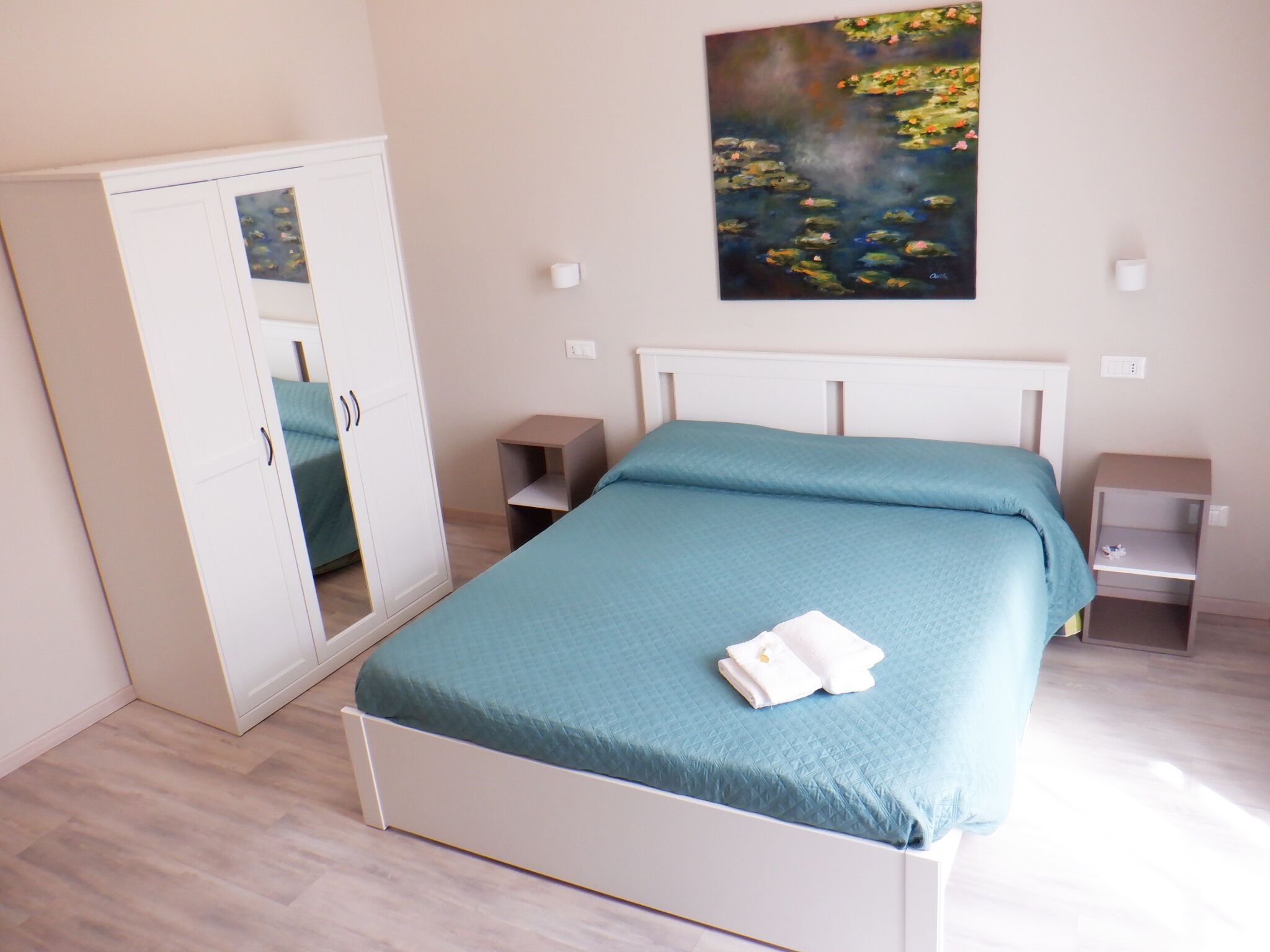 A bedroom with a bed, a wardrobe, bedside tables, and a painting on the wall.