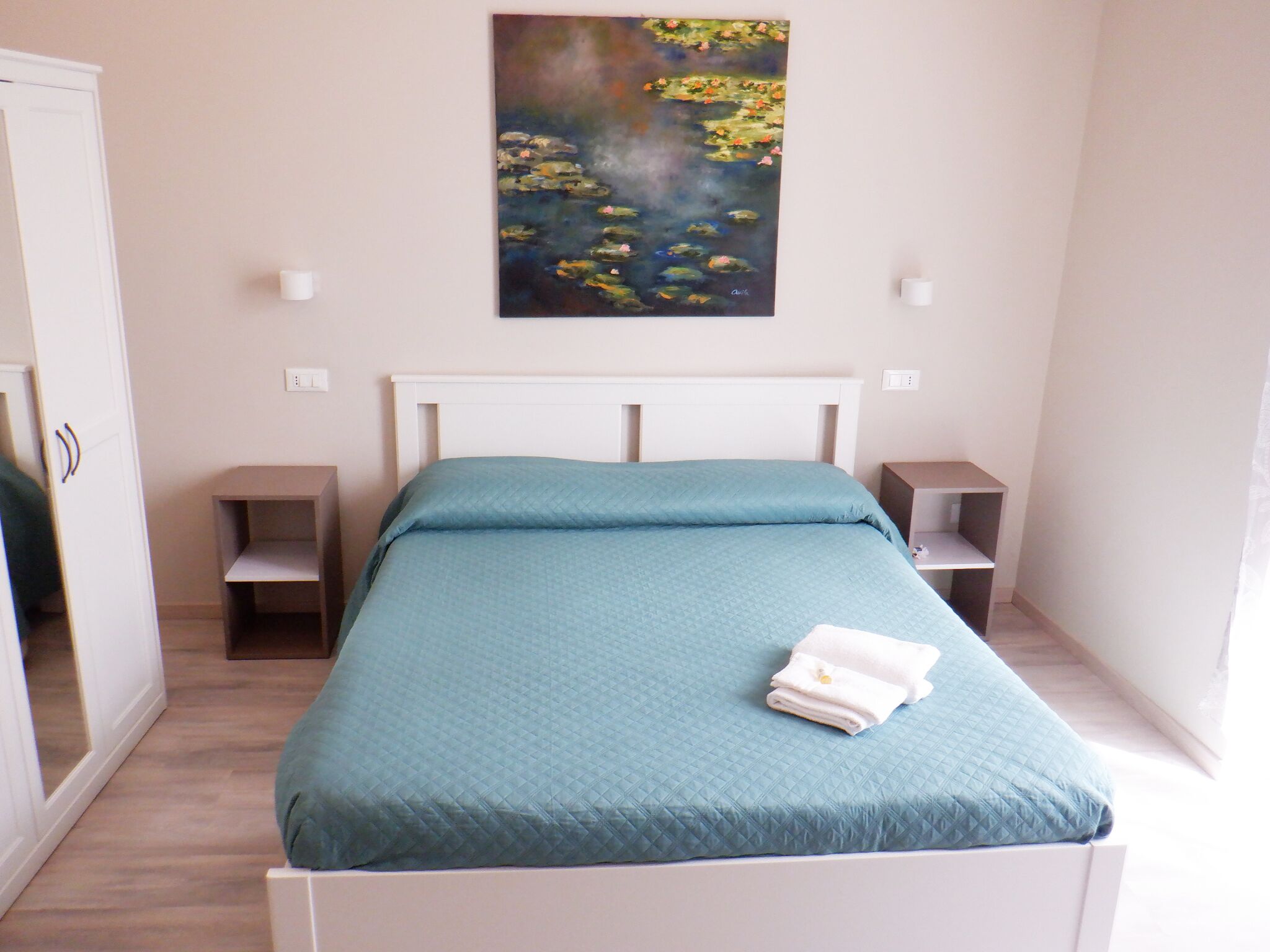 Un dormitorio con cama, un cuadro de nenúfares y un armario blanco.