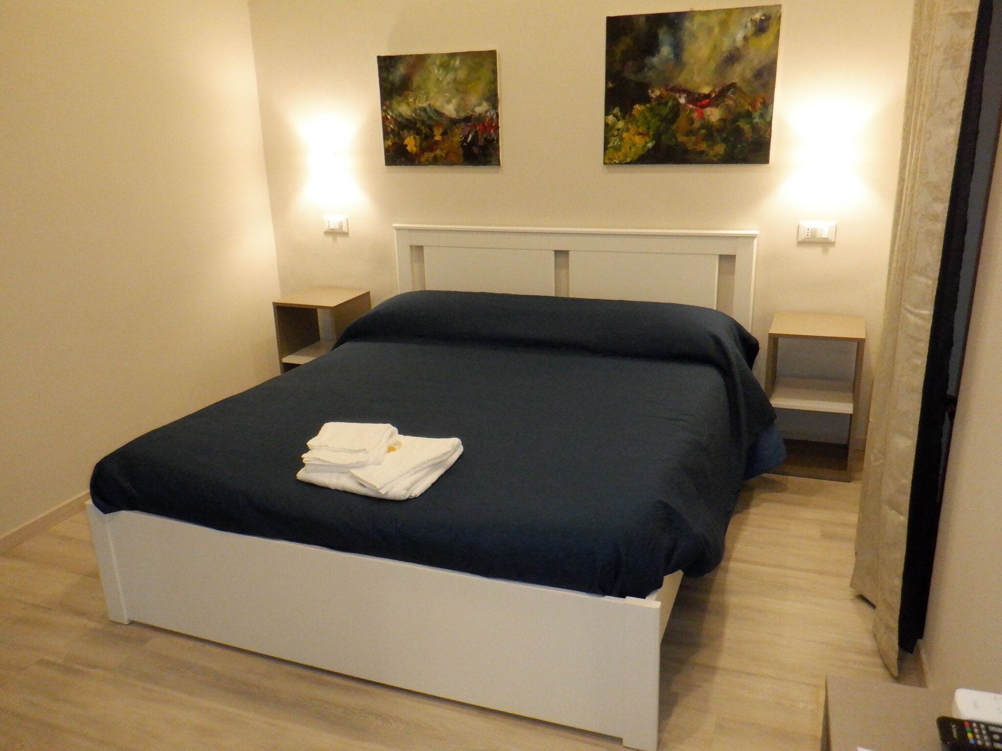 A neatly made bed with a folded towel, a white headboard, and two wall-mounted light fixtures.
