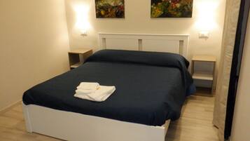 A neatly made bed with a folded towel, a white headboard, and two wall-mounted light fixtures.