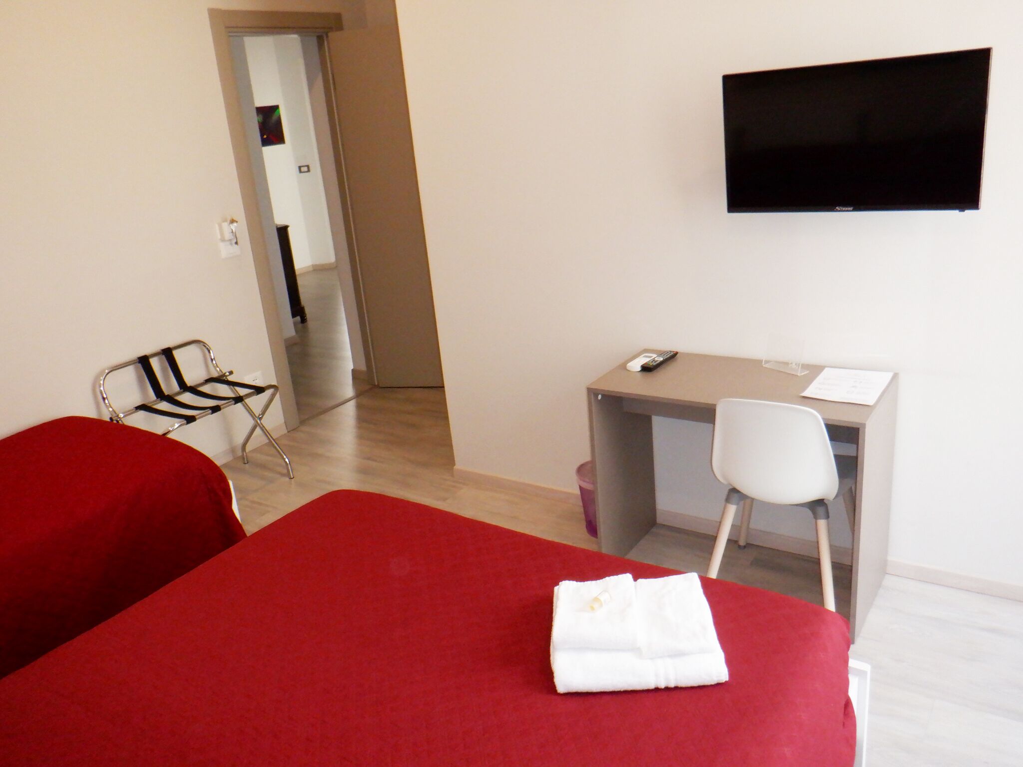 A hotel room with a bed, a desk, a chair, a television, and a red carpet.