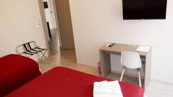 A hotel room with a bed, a desk, a chair, a television, and a red carpet.