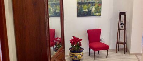 Una habitación con piso de madera, una silla roja, un perchero alto de madera, un espejo grande y un cuadro en la pared.