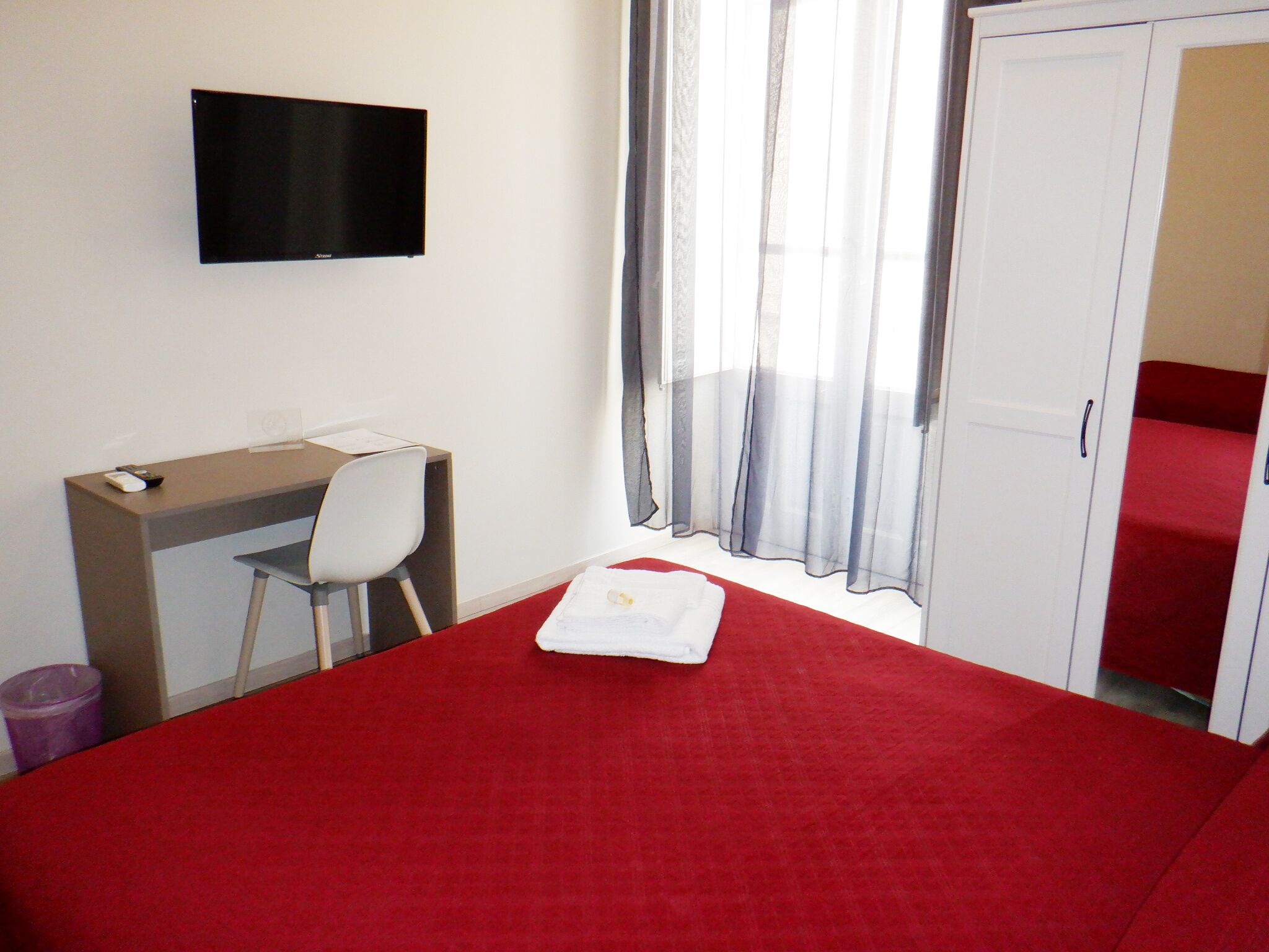 Ett hotellrum med en säng, ett skrivbord, en stol, en tv och en garderob.