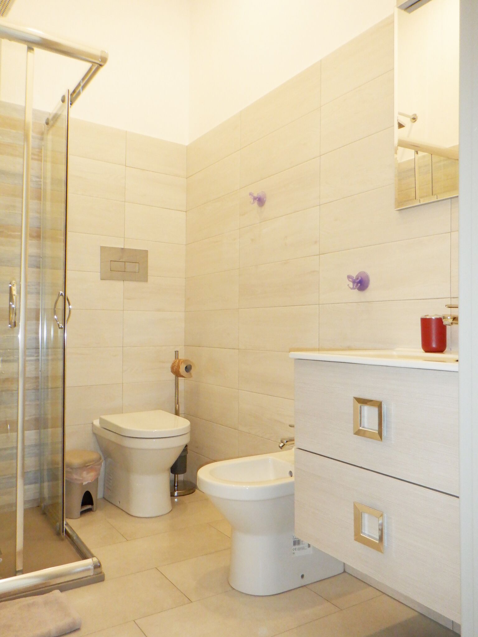 A bathroom with a glass shower enclosure, a toilet, a bidet, and a vanity with drawers.