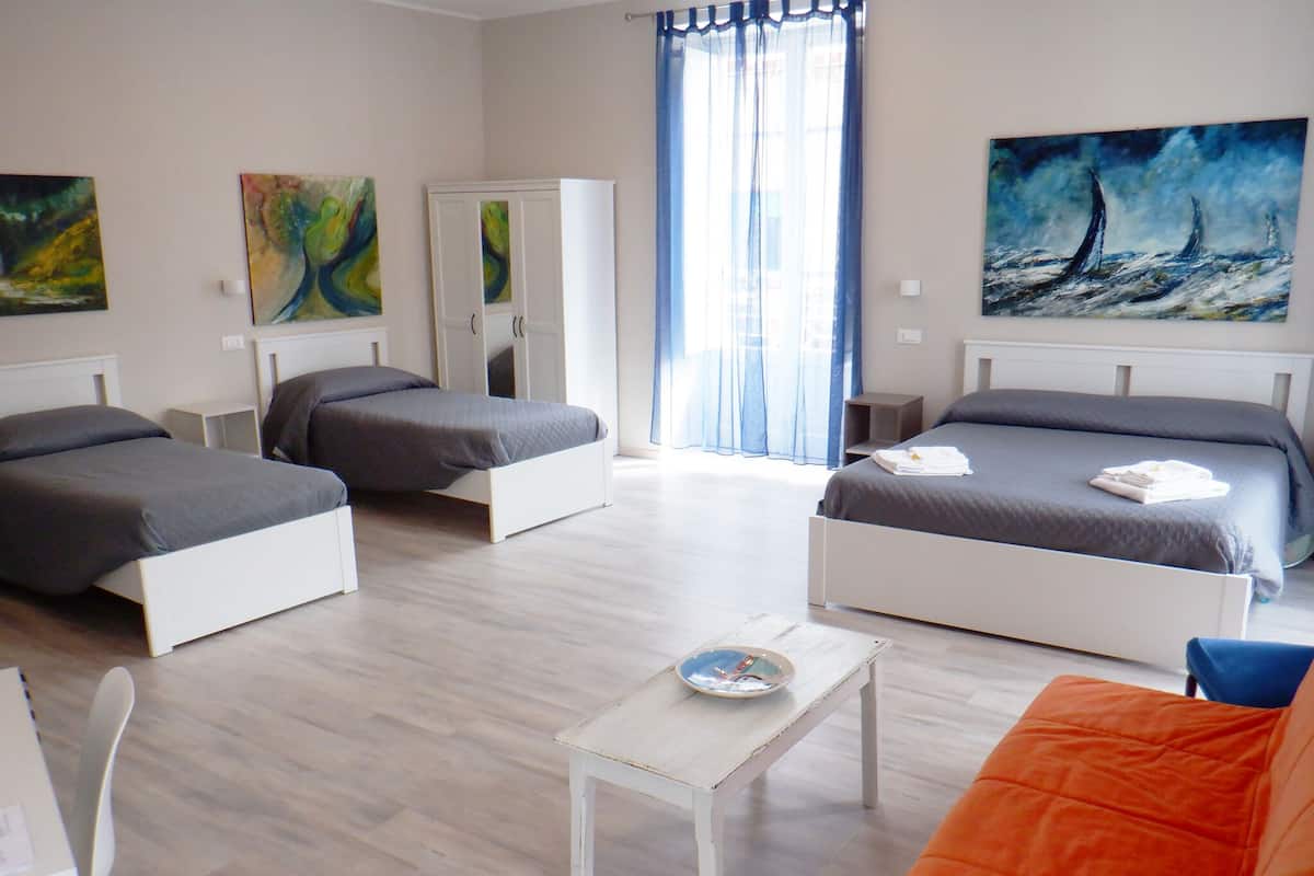 A hotel room with two single beds, a double bed, a small table with a plate, and a colorful painting on the wall.