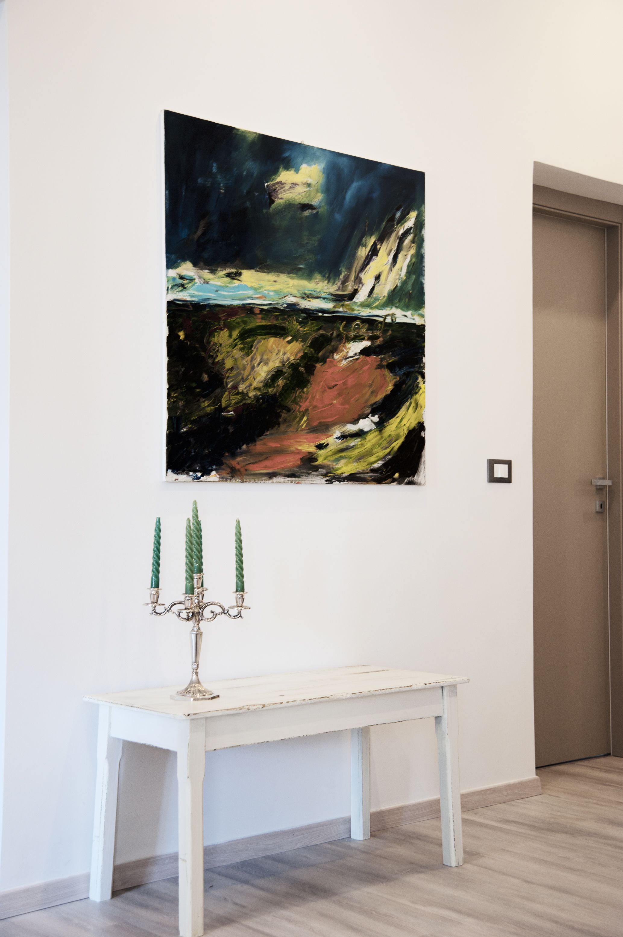 A white table with a green candelabra against a wall with a large abstract painting.