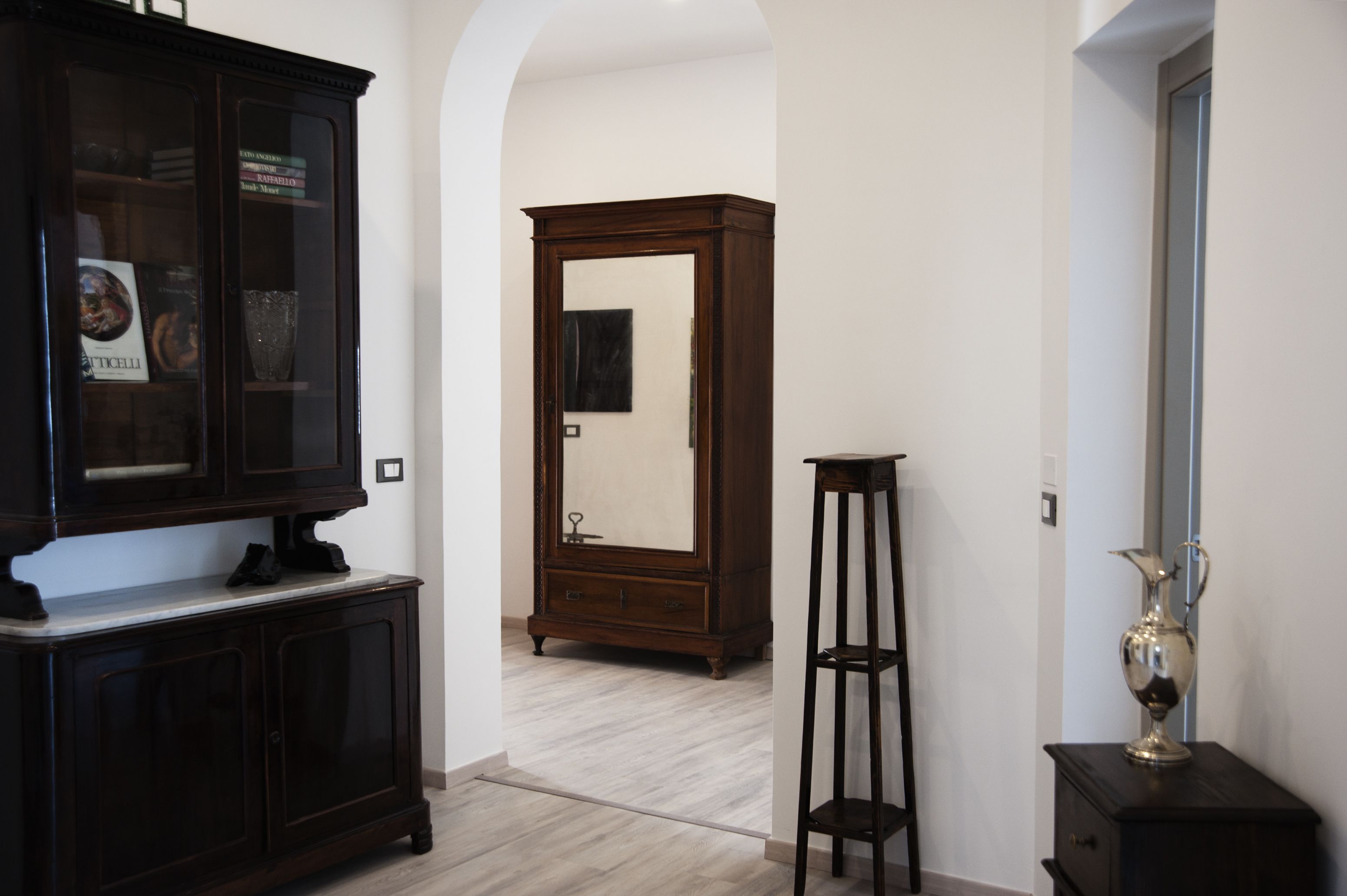 Un pasillo con un mueble de madera oscura, un espejo alto y una mesita con un jarrón.