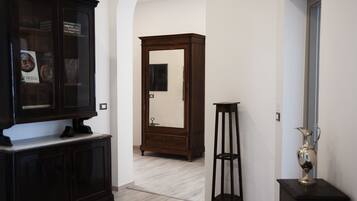Un pasillo con un mueble de madera oscura, un espejo alto y una mesita con un jarrón.